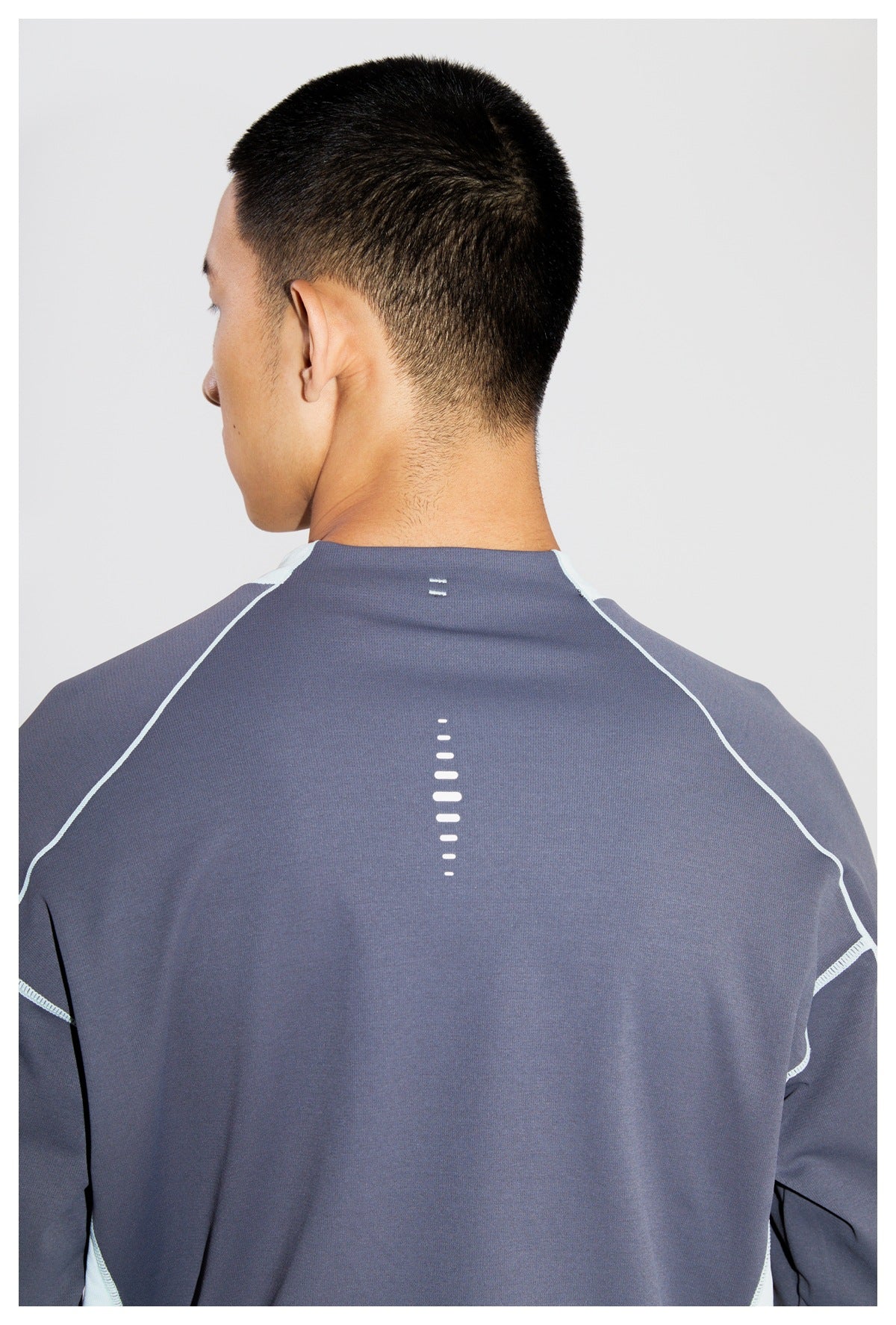 Close back view of a model wearing a charcoal top with pale aqua piping and reflective dashes.