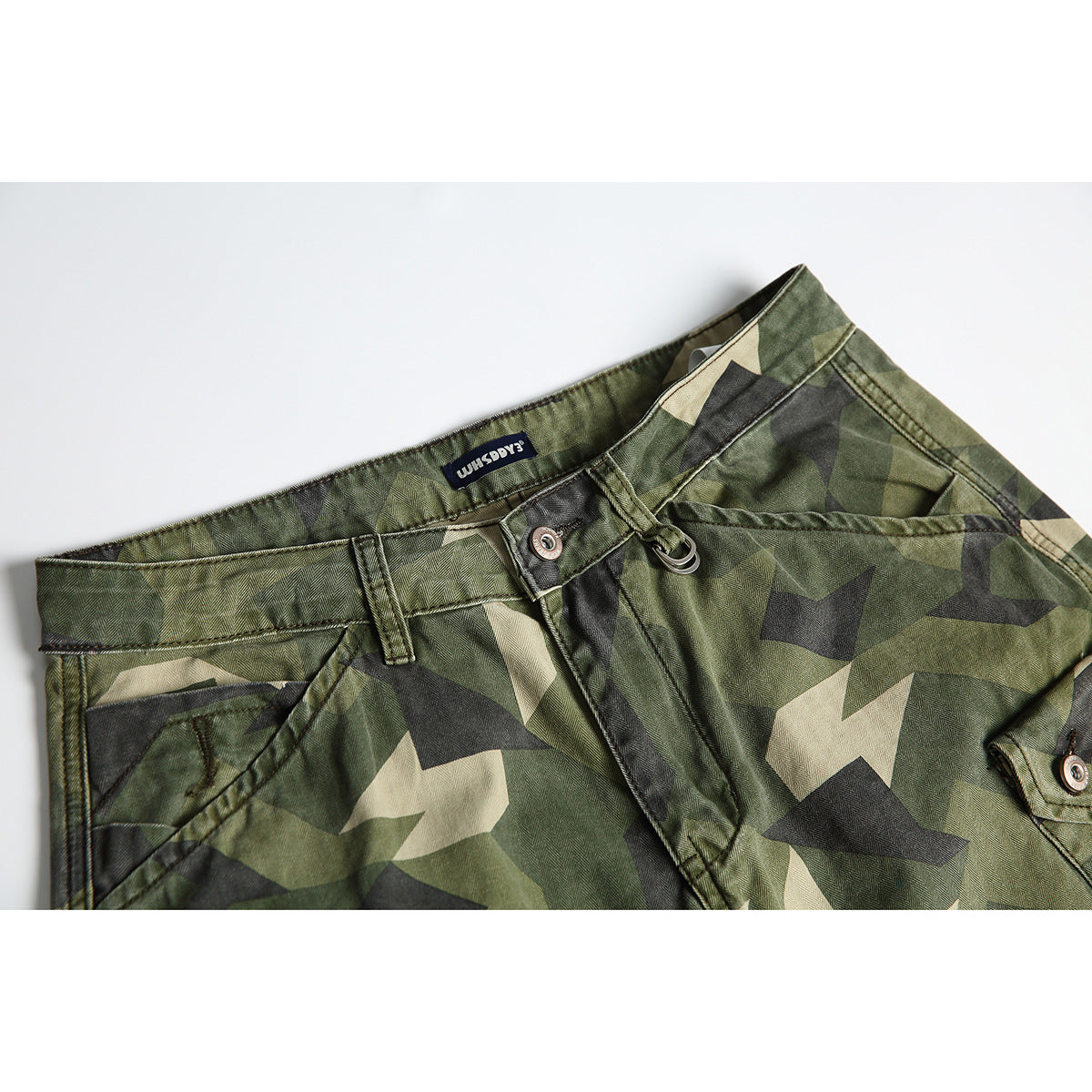 Close-up of green camouflage trousers showing the waistband, belt loop, button, and front pocket.