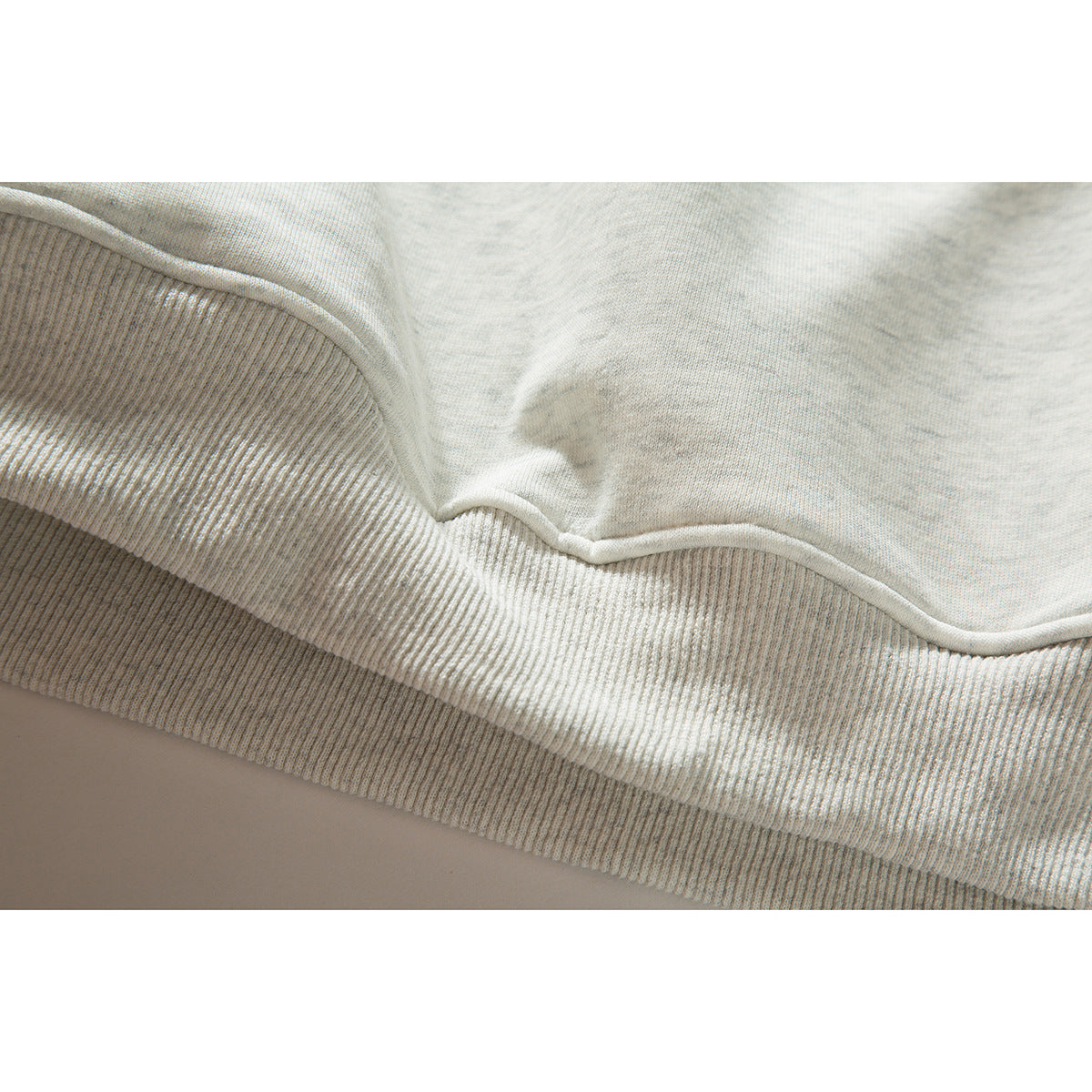Close-up of the off-white sweatshirt's ribbed hem and stitched lower edge.