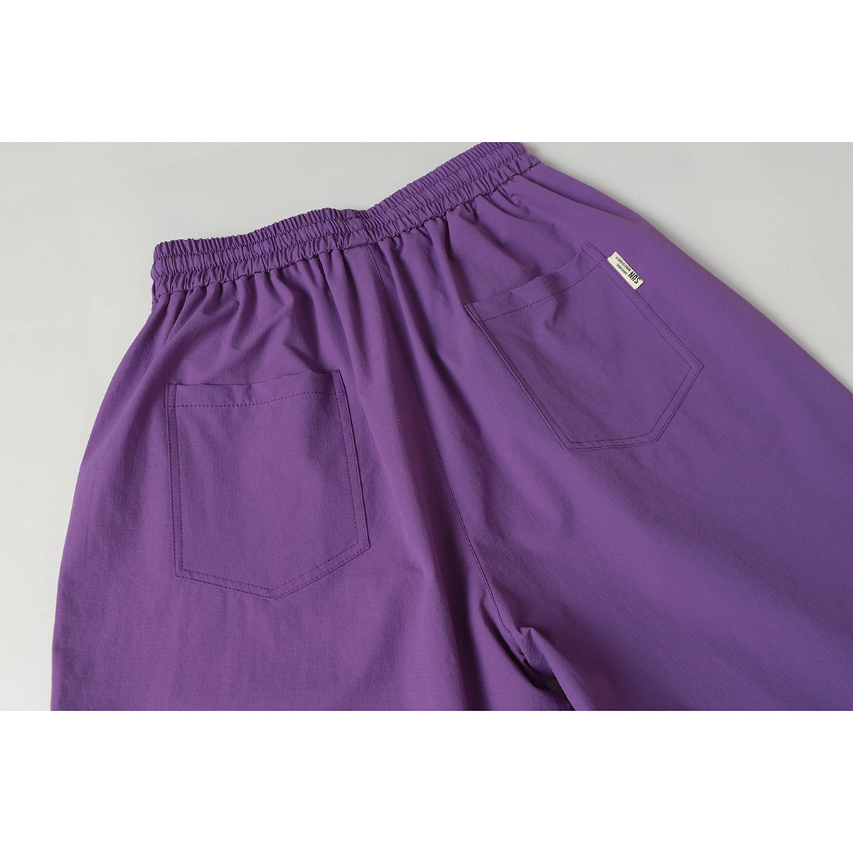 Back view of purple pants with a gathered elastic waistband and two patch pockets.