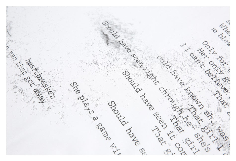 Close-up of distressed black English text artwork printed on white fabric.