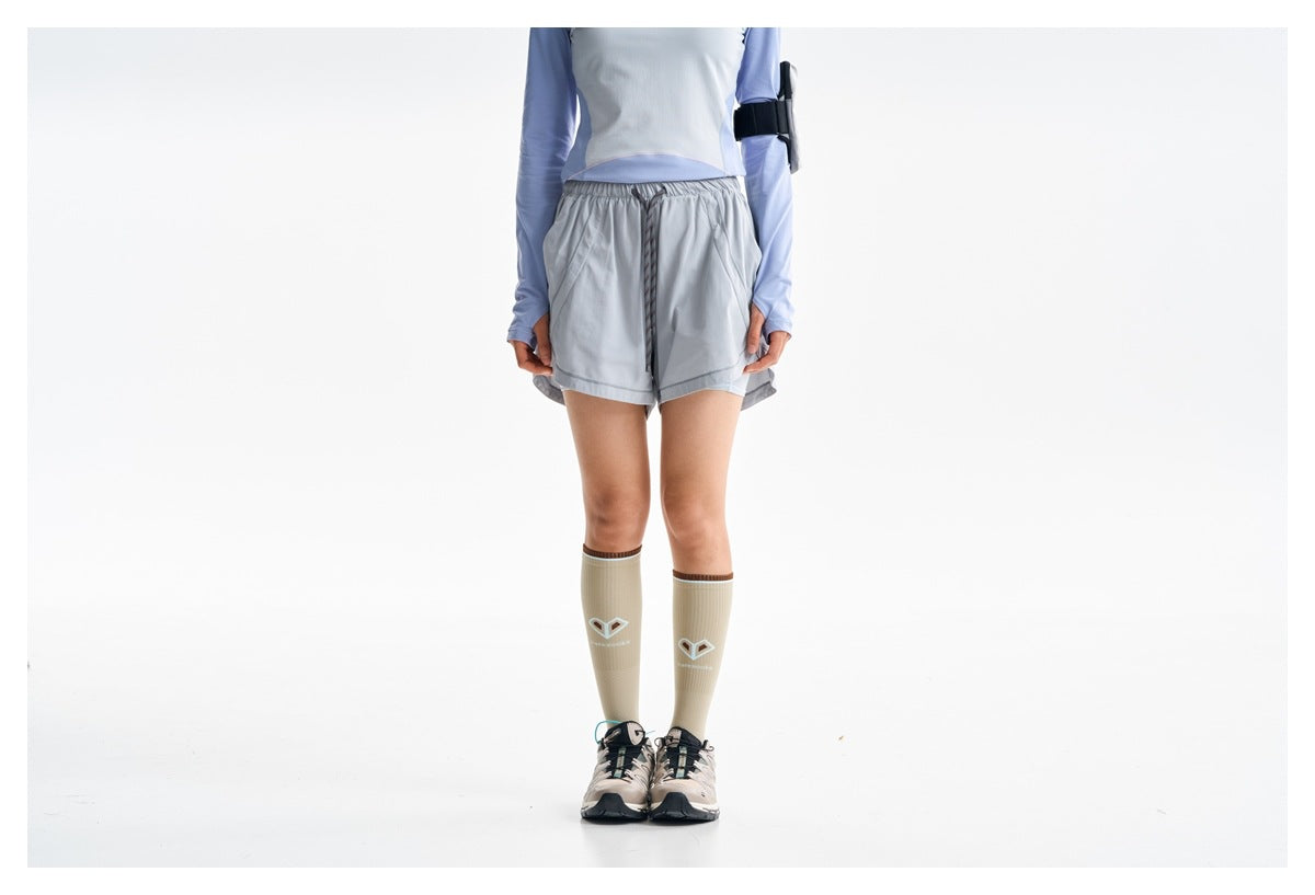 Cropped view of a model wearing gray running shorts with a dark drawstring and a lavender long-sleeve top.