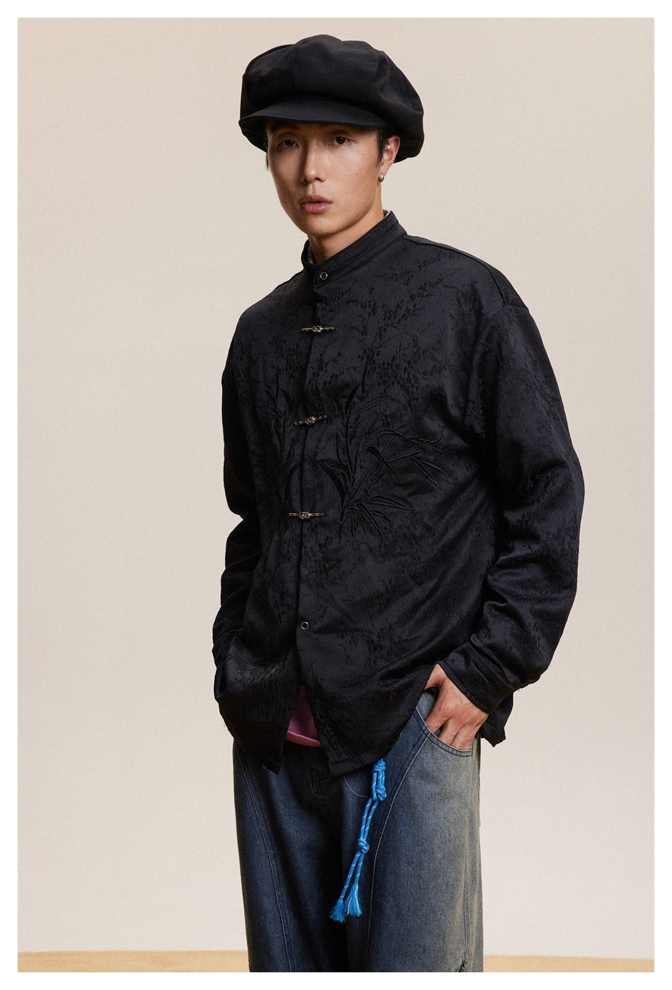 Model wearing a black textured jacket with stand collar, frog closures, and tonal front embroidery.
