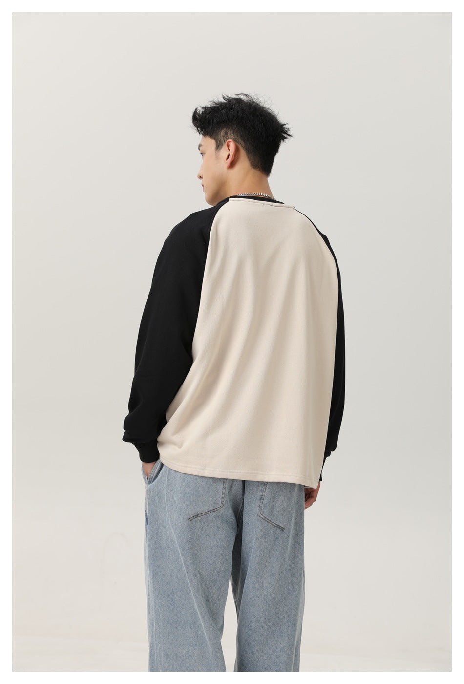 Cropped rear view of a model wearing a cream sweatshirt with black raglan sleeves and light-wash jeans.
