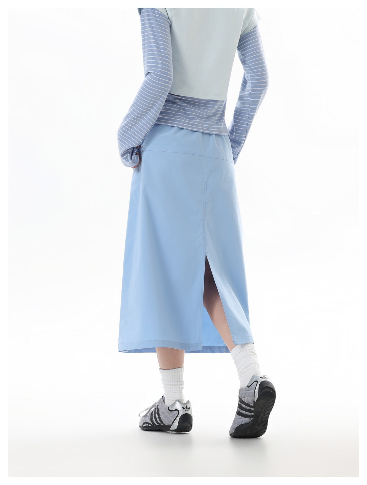 Back view of a model wearing a light blue midi skirt with a high side slit and a pale blue top with striped sleeves.