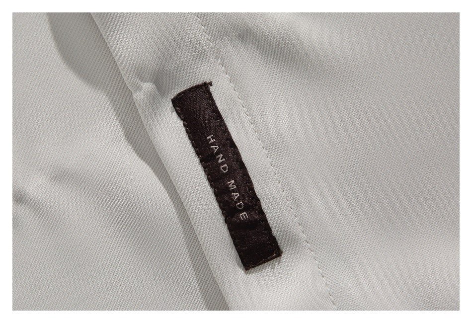 Close-up of a dark sewn label reading HAND MADE on the ivory shirt.