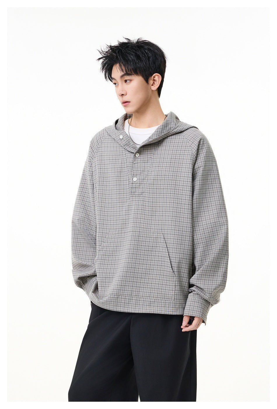Model wearing a gray checked hooded pullover with a buttoned neckline and black trousers, shown from the front.