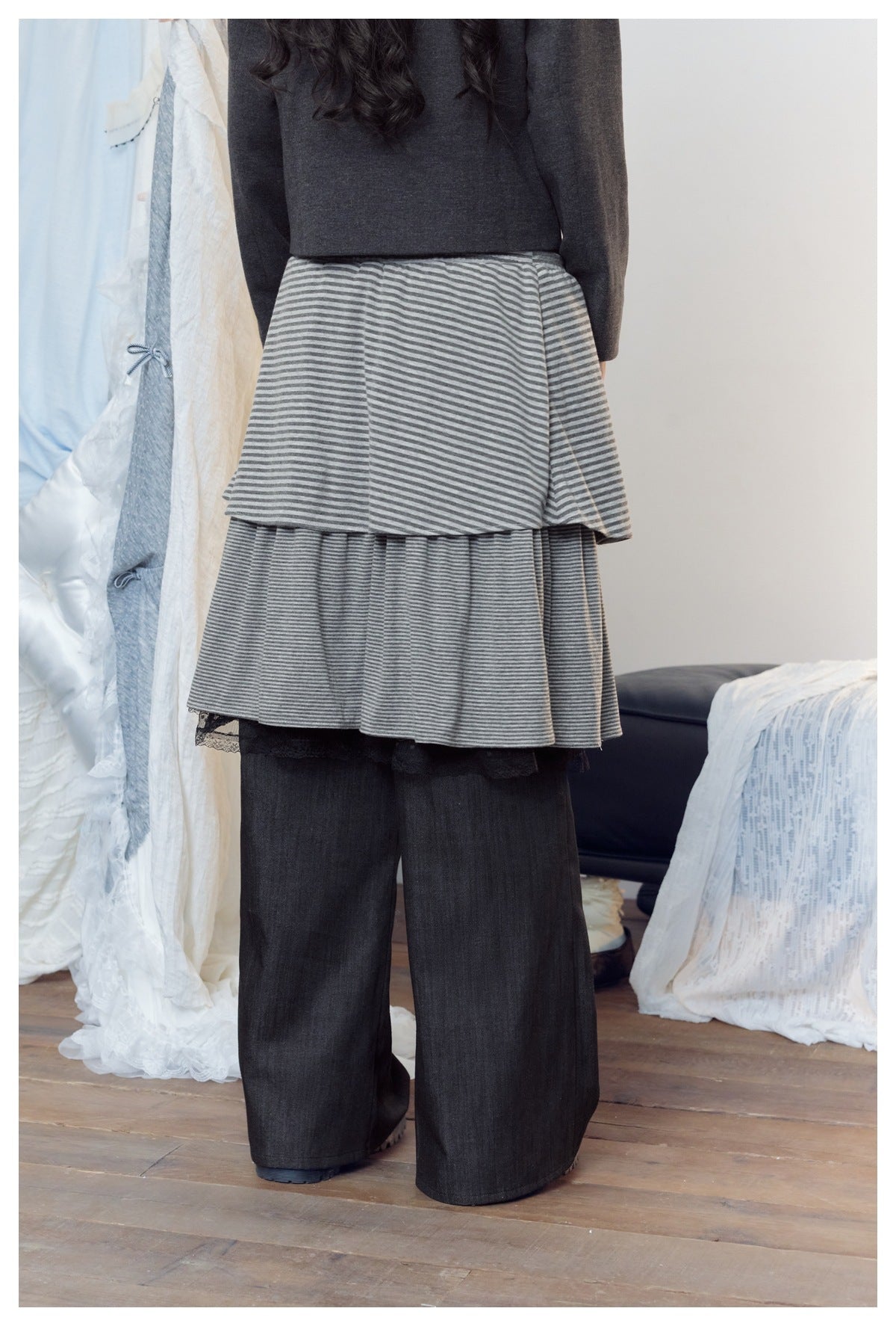Back view of a model wearing a gray striped tiered skirt with black lace trim over wide black pants.