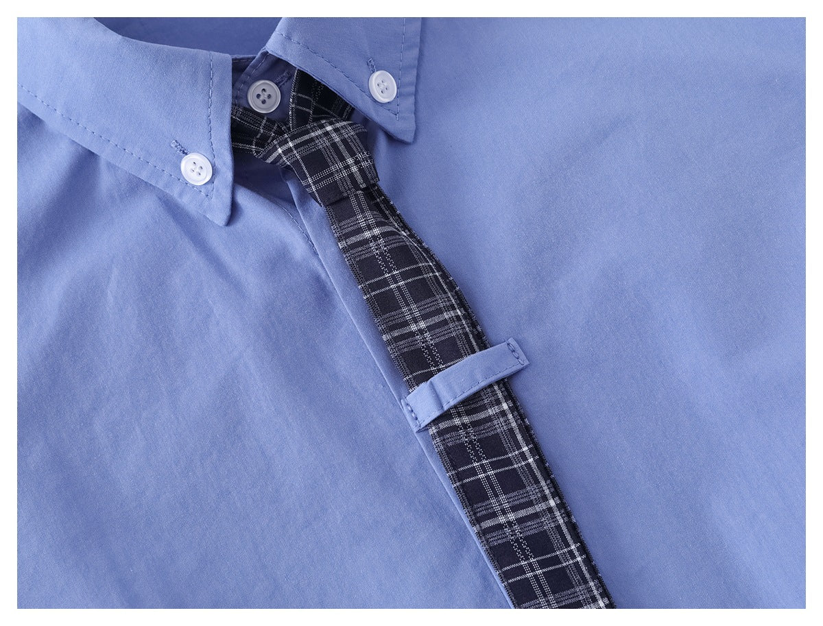 Close-up of a black plaid tie against a light blue shirt, secured by a matching fabric loop.