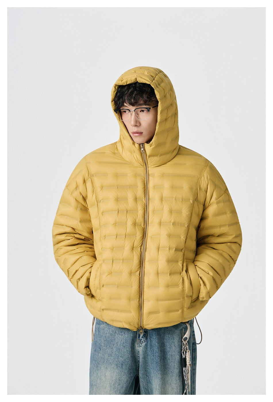 Front view of a model wearing a zipped mustard-yellow hooded quilted jacket with hands in the pockets.