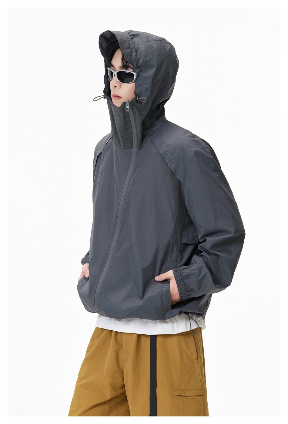 Side view of a model wearing a charcoal hooded jacket zipped high over the face, with the hood up.