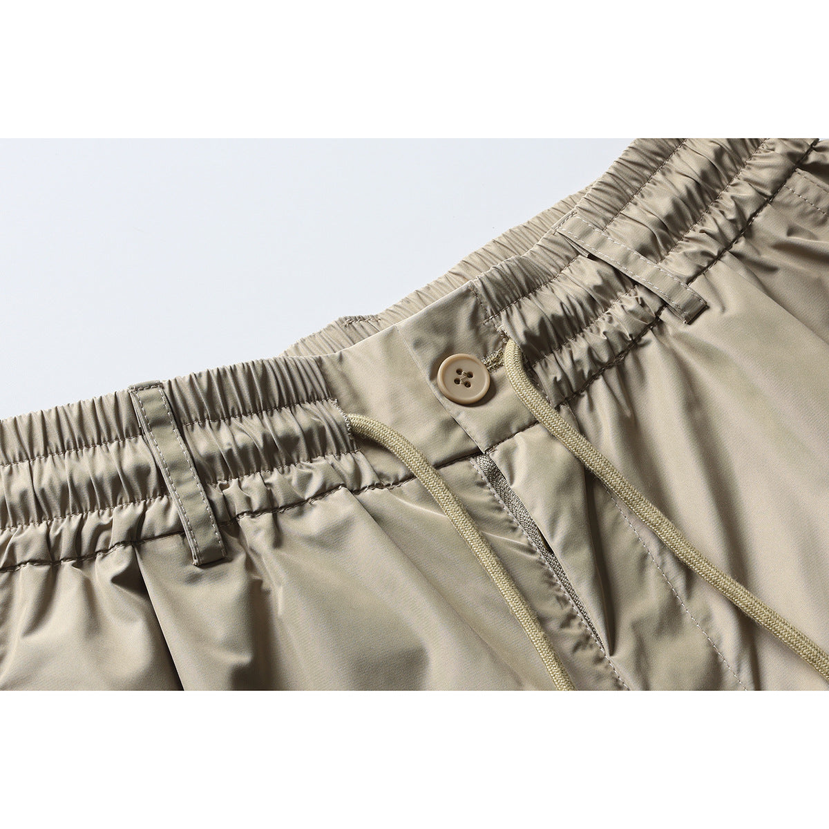 Close-up of beige trousers with an elastic waistband, belt loops, button, and braided drawstrings.