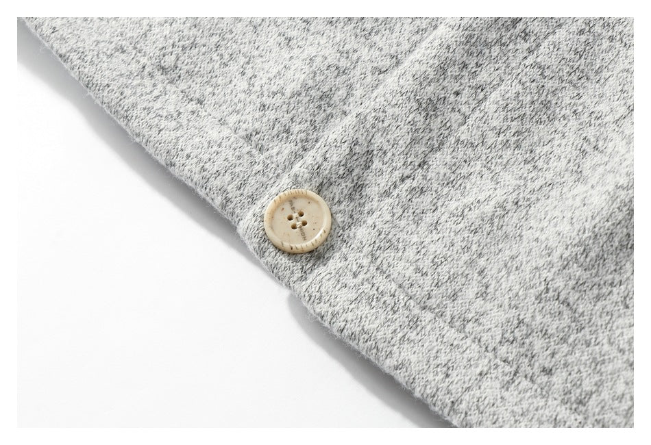 Cream four-hole button attached near the edge of light gray marled knit fabric.