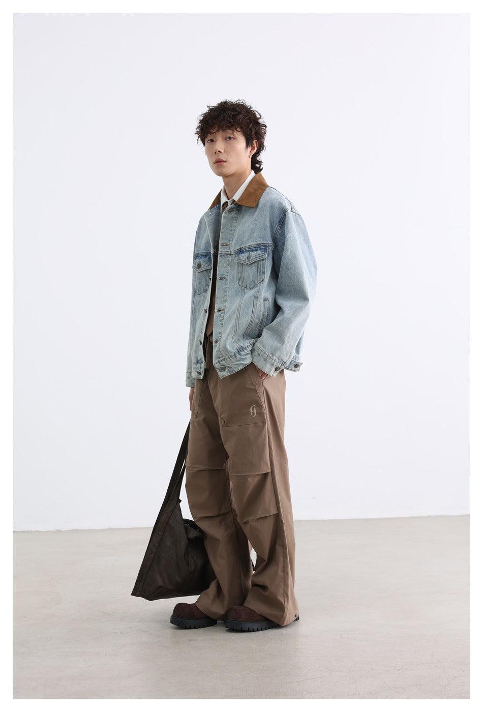 Model in a three-quarter pose wearing a light blue denim jacket with brown collar, hand in pocket, with brown pants
