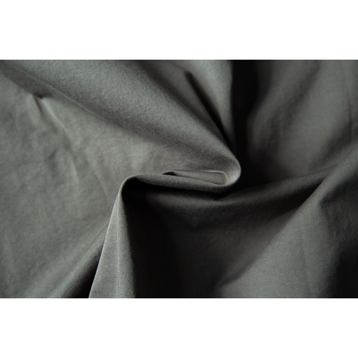 Close-up showing the gray-green shirt fabric draped into folds and its fine surface texture.