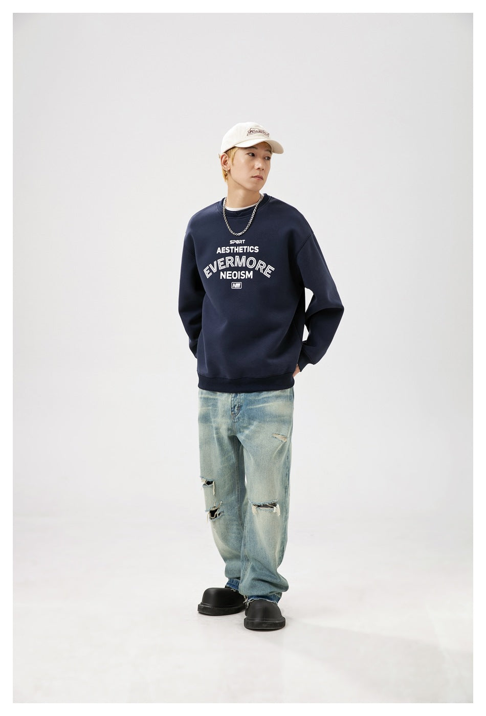 Model in a navy graphic crewneck sweatshirt, shown at a slight angle with distressed light-wash jeans.