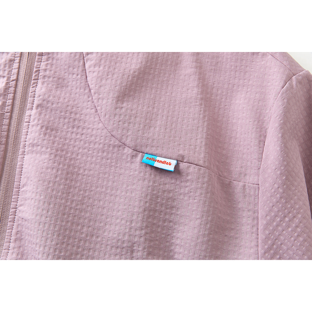 Close-up of the mauve jacket's textured chest panel and a small blue-and-white fabric label.