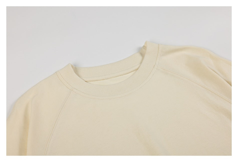 Close-up of an ivory sweatshirt’s ribbed crew neckline and raglan shoulder seams.