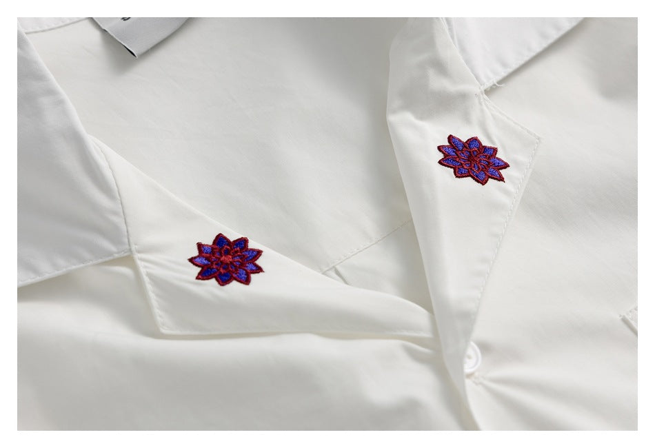 Close-up of a white shirt with two red-and-blue embroidered flowers on the collar.