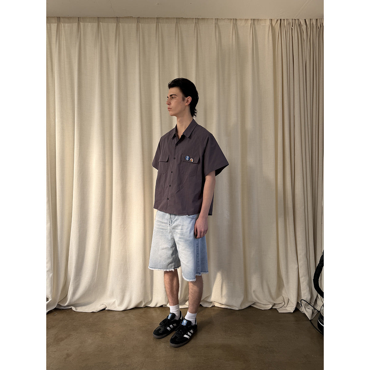 Full-length side view of a model wearing a charcoal button-up shirt, light denim shorts, white socks and black sneakers.