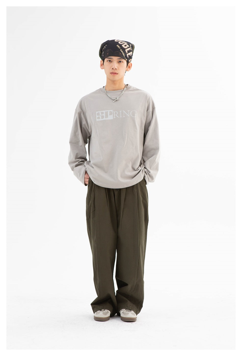 Full-length front view of a model wearing a gray oversized long-sleeve shirt with pale lettering and olive trousers.