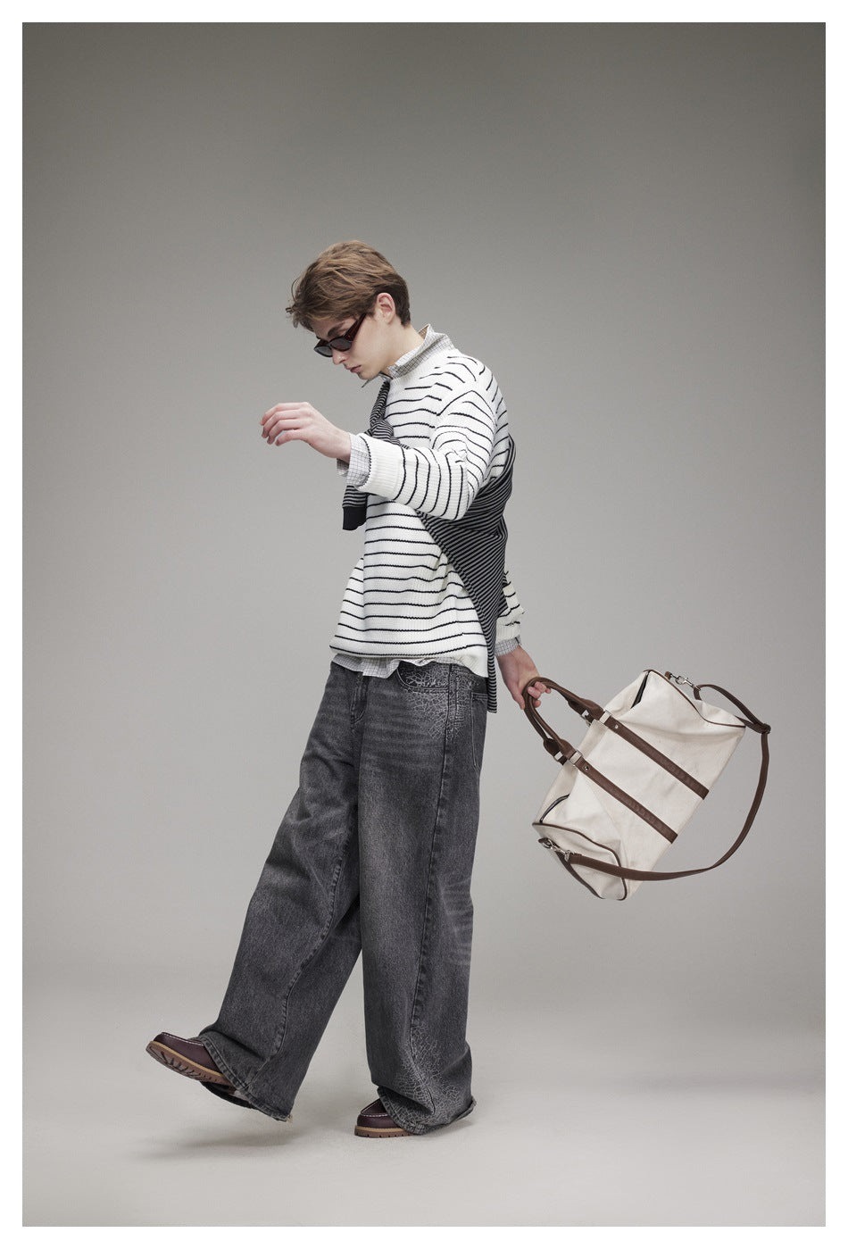 Model wearing a white sweater with thin black stripes and a dark striped knit draped diagonally across it, with wide gray