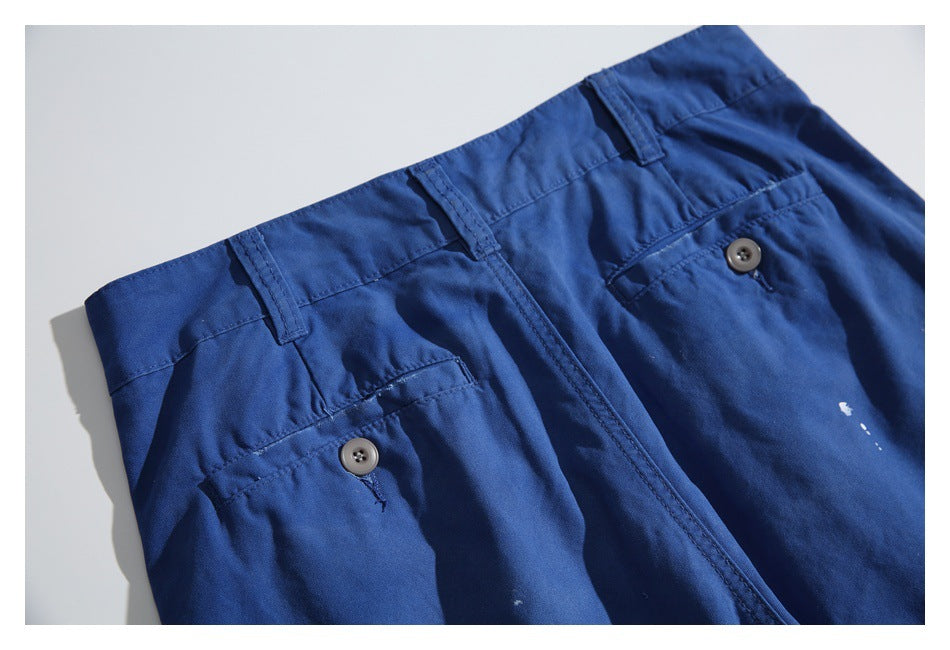 Close-up of the waistband, belt loops, fly, and buttoned pockets on royal-blue trousers.