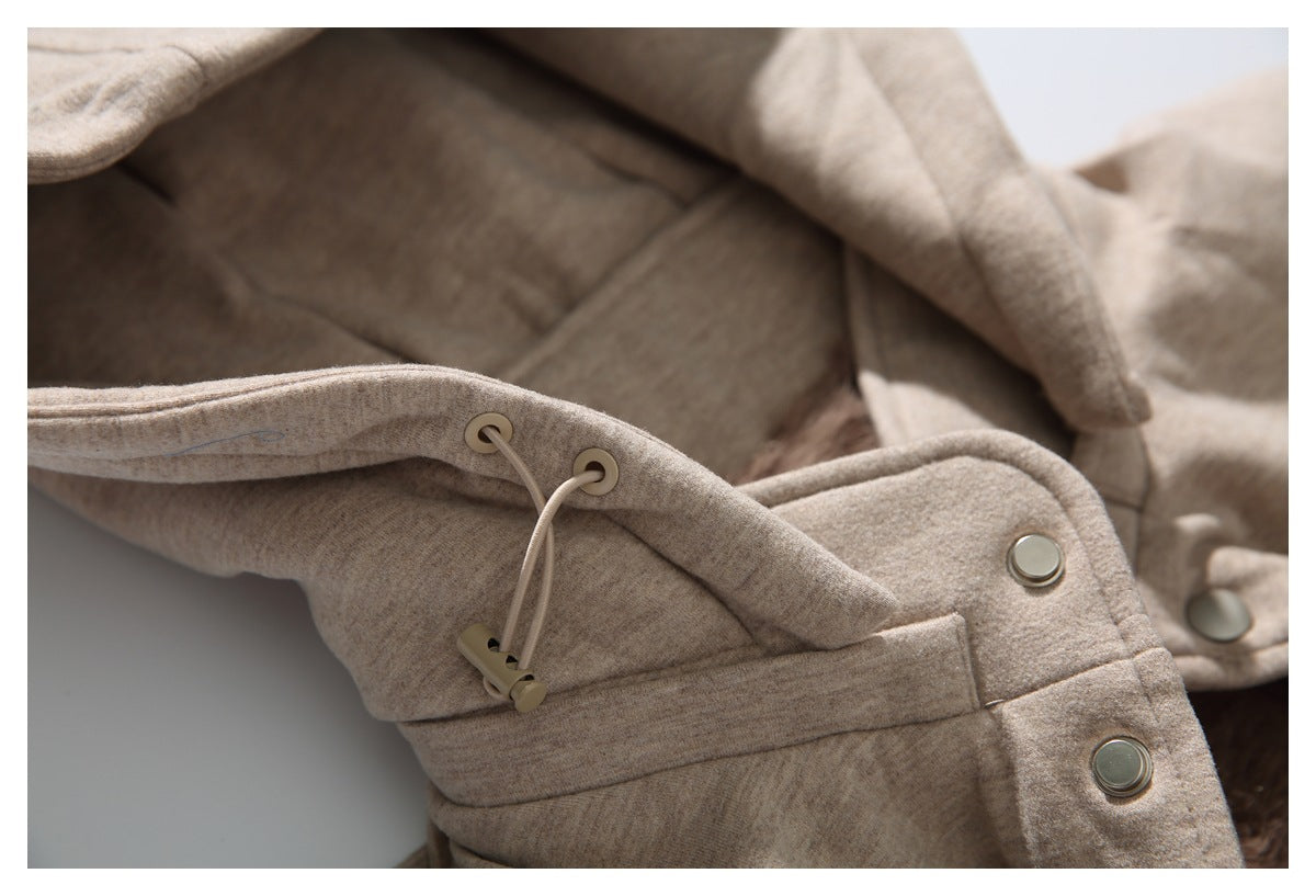 Close-up of a beige hooded jacket showing drawcord eyelets, toggles, and silver-tone snaps.