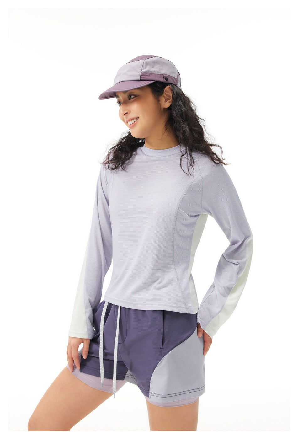 Three-quarter side view of a woman wearing a pale lavender long-sleeve top with light sleeve panels and color-block shorts.