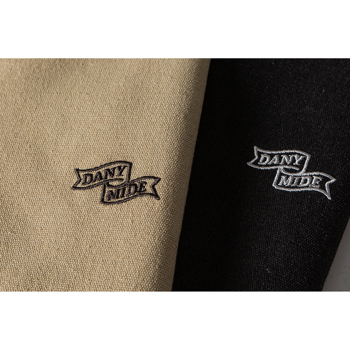 Close-up of embroidered banner-shaped logos on beige and black garment fabric.