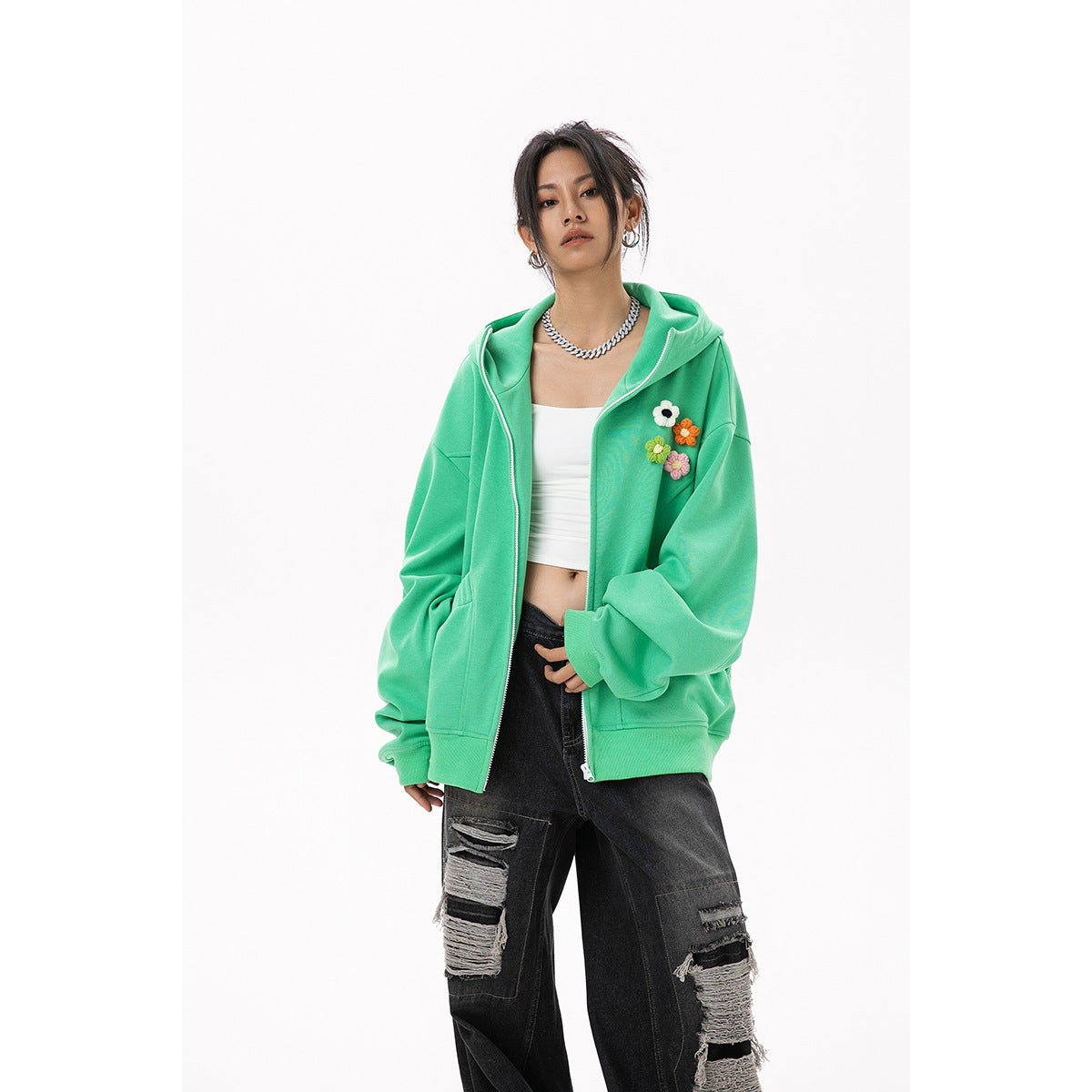 Model wearing an oversized mint-green zip hoodie with colorful flower appliqués, paired with distressed black jeans.
