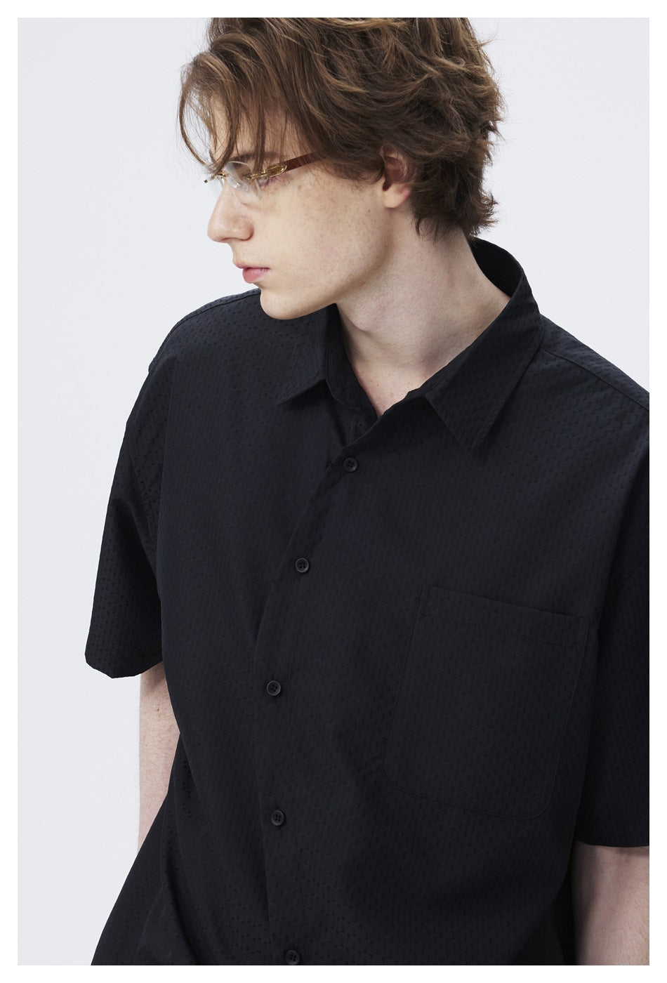 Close-up of a black short-sleeve shirt showing its subtle textured pattern, pointed collar, buttons, and chest pocket.
