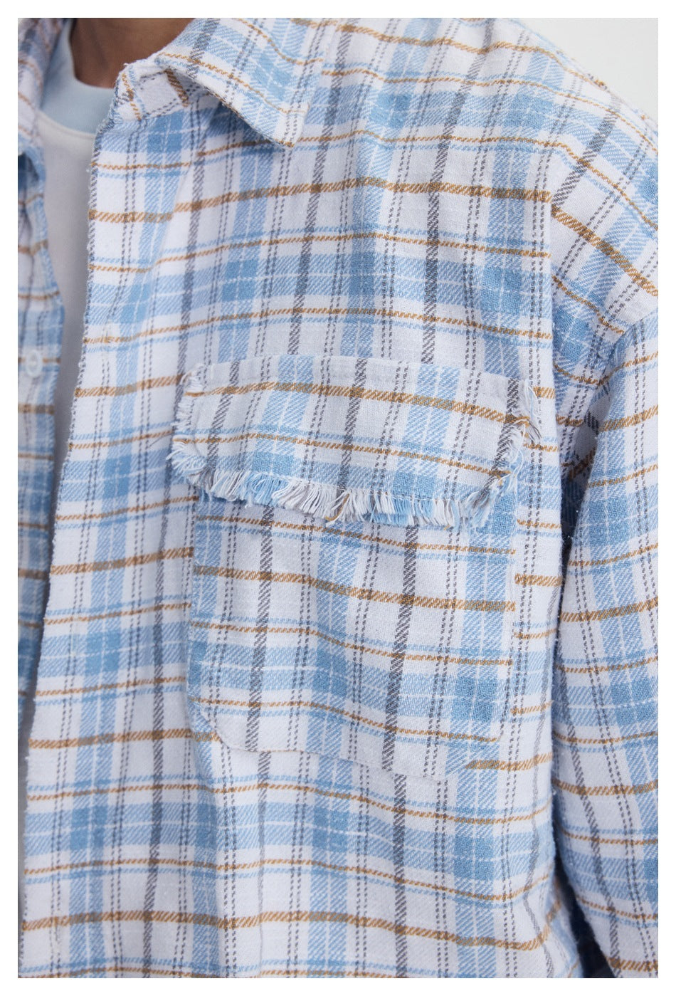 Close-up of the light blue plaid shirt's chest pocket with a frayed flap and edges.
