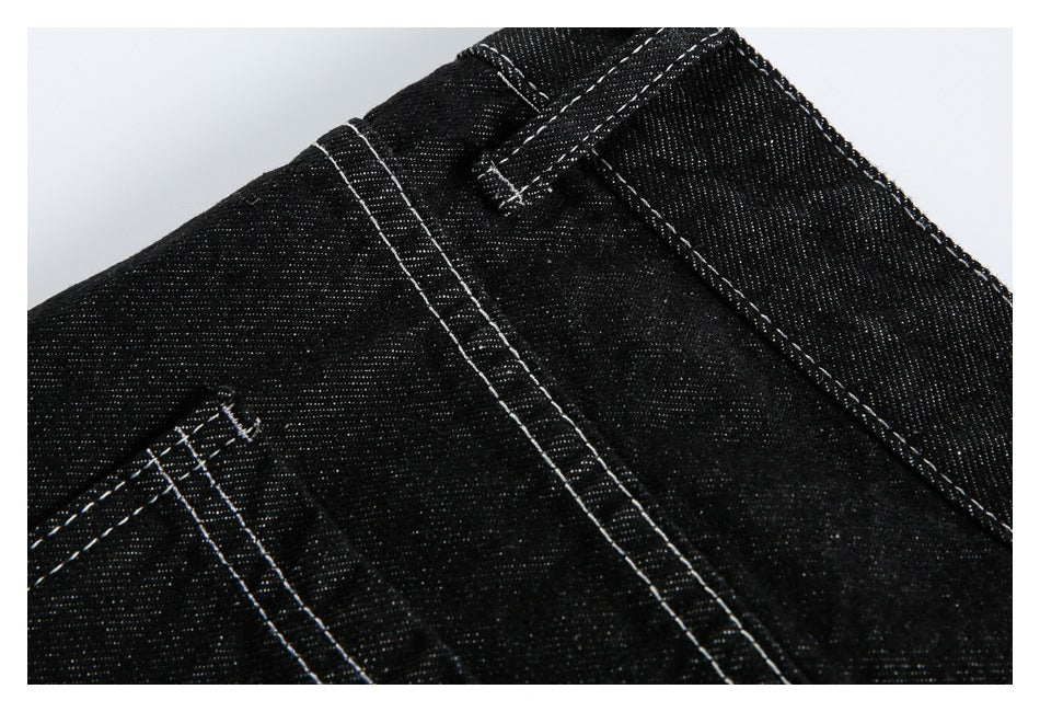 Close-up of black denim waistband, belt loop, and seams with white stitching.