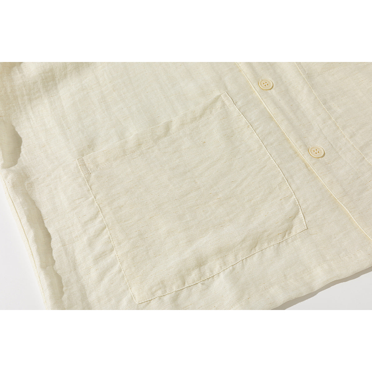 Close-up of a large patch pocket and two ivory buttons on an ivory shirt.