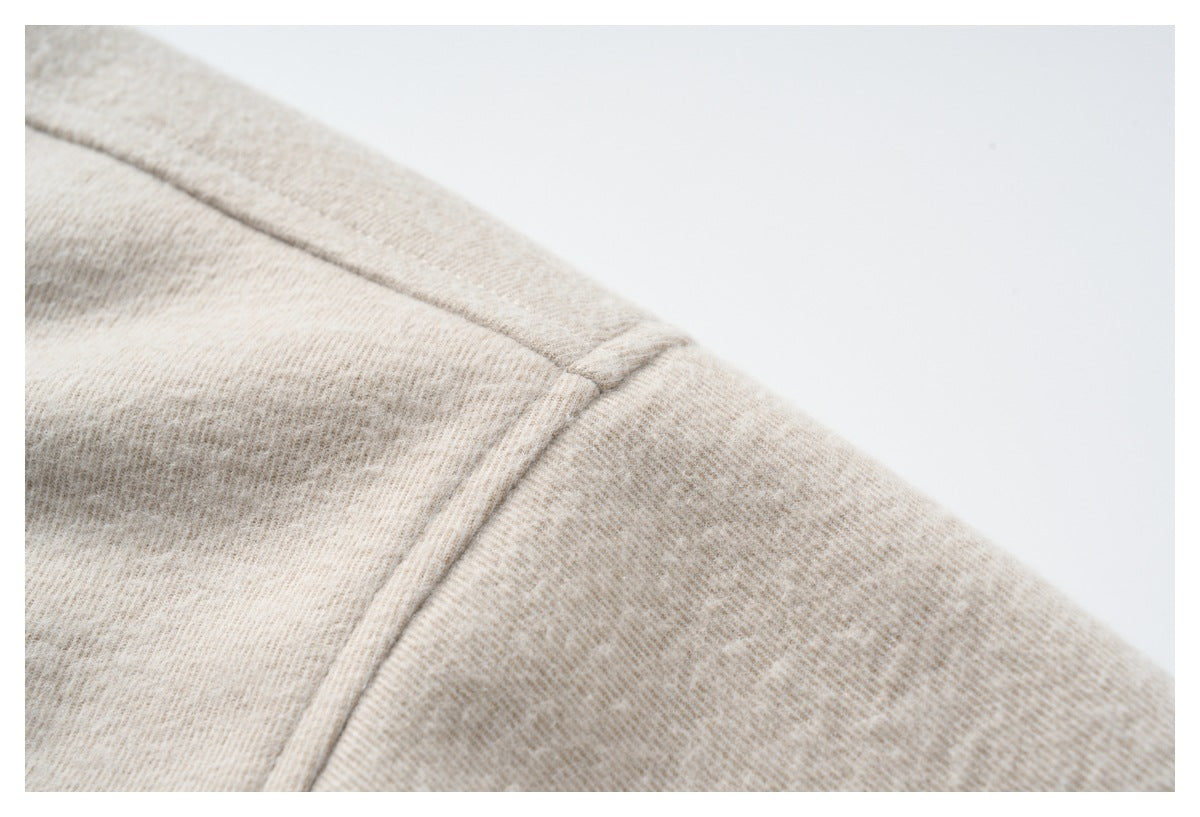 Close-up of beige heathered fabric and a stitched shoulder seam against a white background.