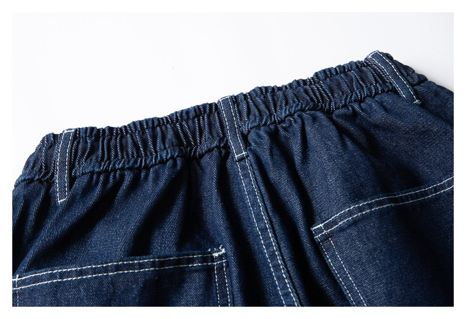 Close-up of the back waistband of dark indigo denim shorts, with elastic gathering, belt loops, and two pockets.
