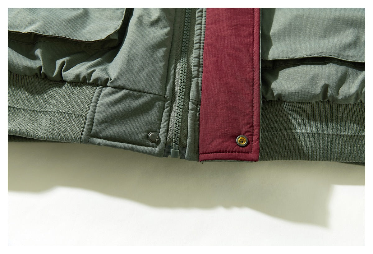 Close-up of the sage green jacket's lower front, zipper, burgundy placket, and ribbed hem.