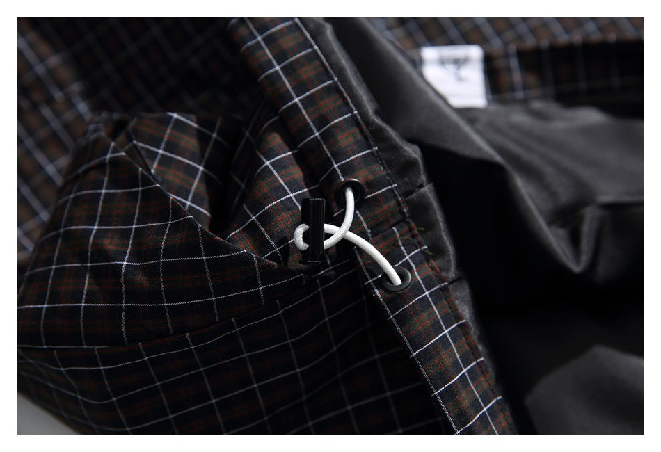 Close-up of a white drawcord and black toggle threaded through dark plaid fabric.