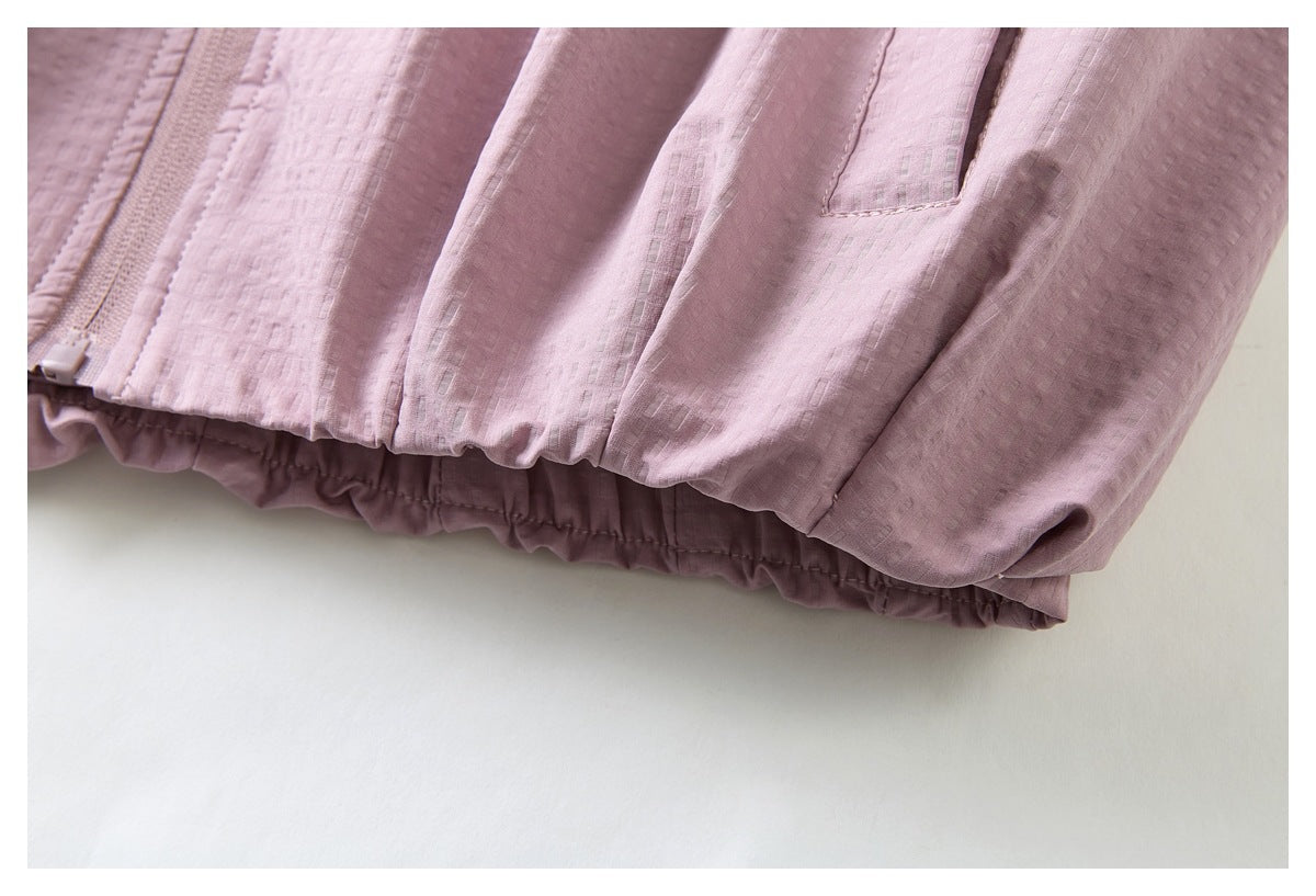 Close-up of a dusty pink jacket’s textured fabric, zipper, pocket edge, and gathered elastic hem.
