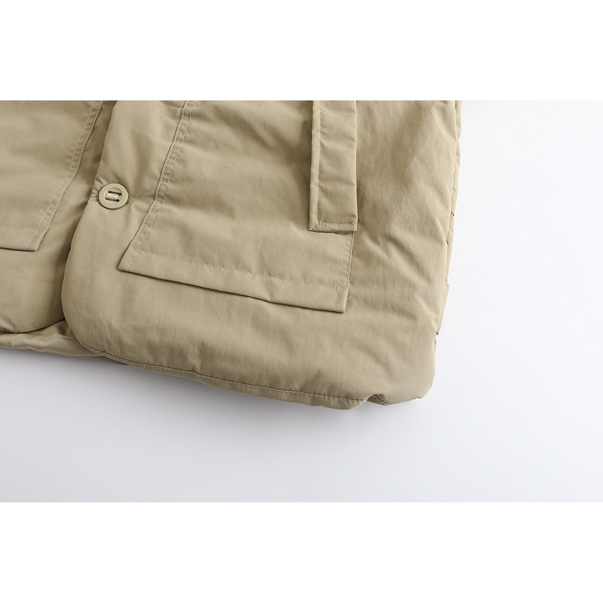 Close-up of the beige jacket’s lower front, showing a flap pocket, button, stitching, and hem.