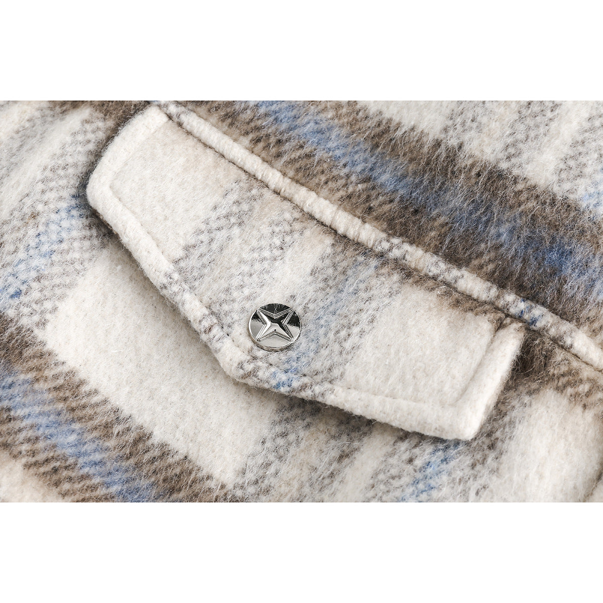 Close-up of a flap pocket with a round silver button on fuzzy cream, gray, and blue plaid fabric.
