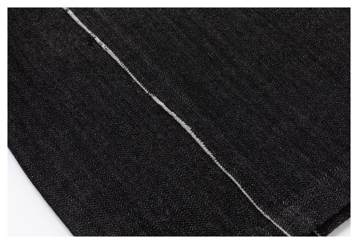 Close-up of black denim with a curved seam finished in pale, frayed edging.