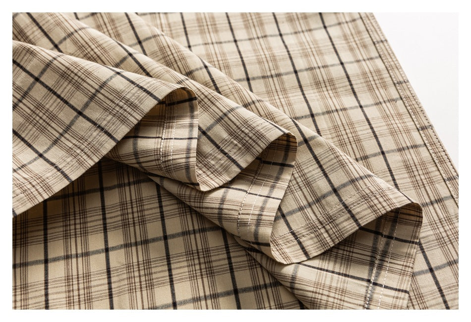 Close-up of the beige plaid shirt's fabric gathered into folds, showing its checked pattern and stitched edge.