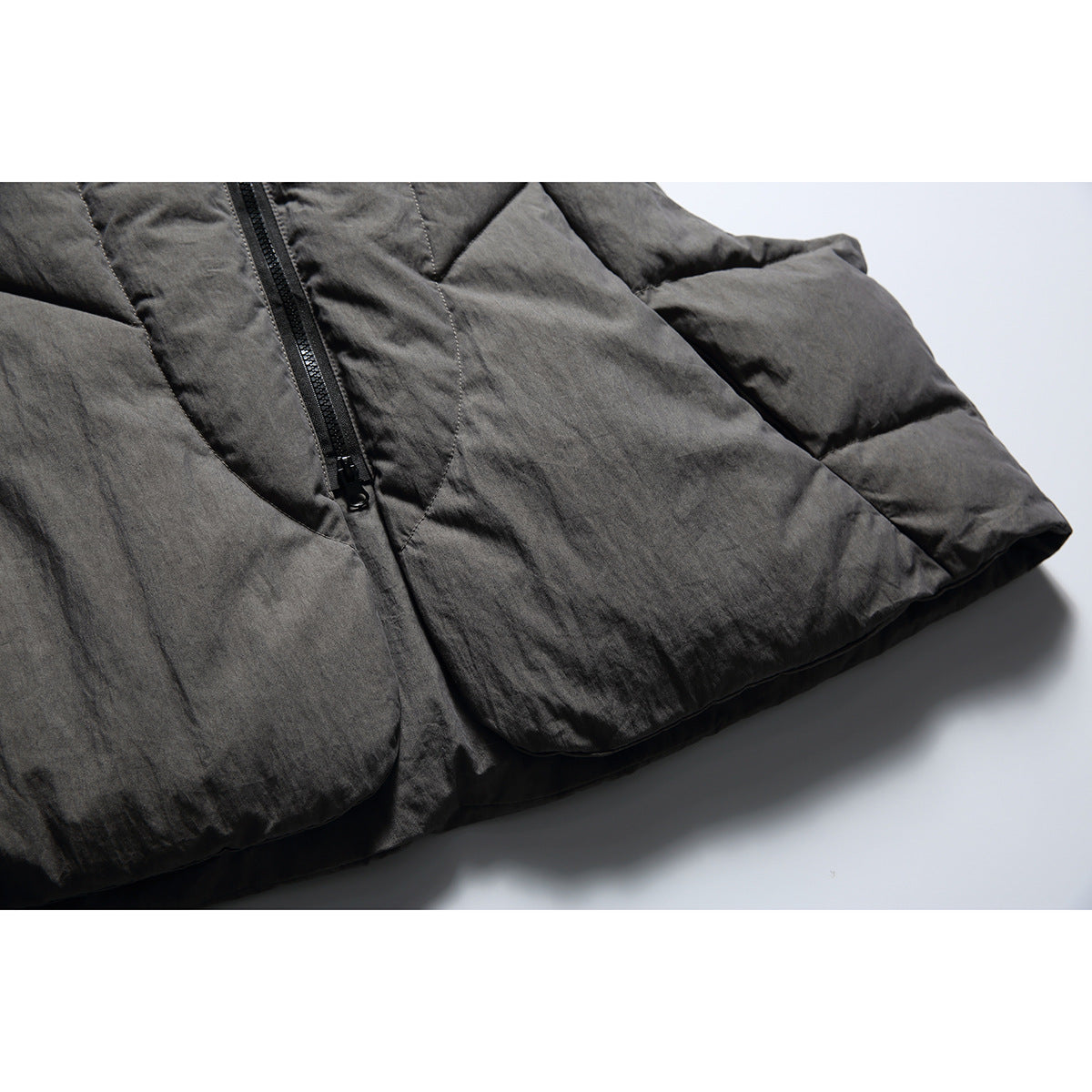 Close-up of the charcoal-gray vest's black zipper, quilted panels, and padded hem.