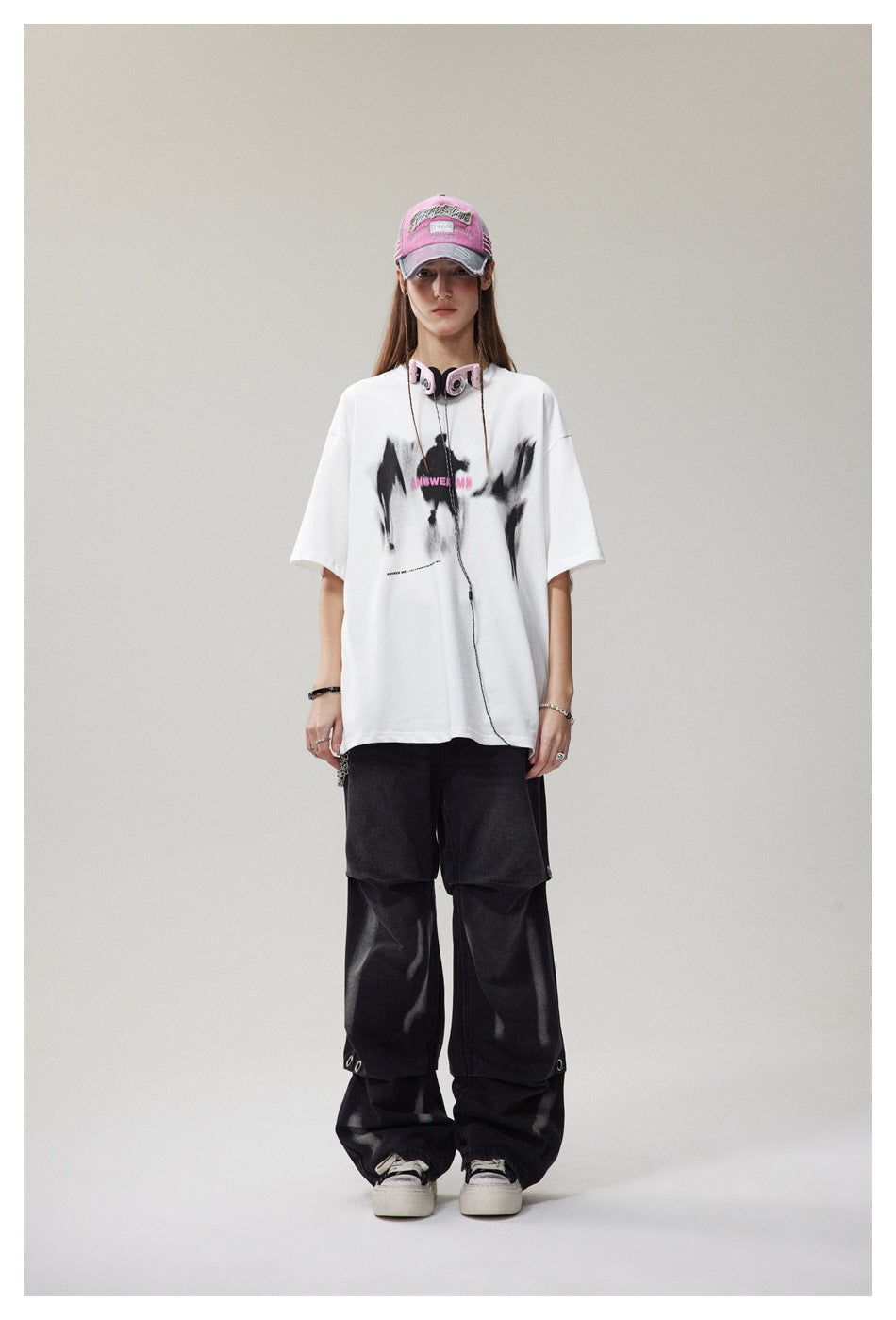 Model wearing an oversized white graphic T-shirt with black and pink front artwork and loose black trousers.