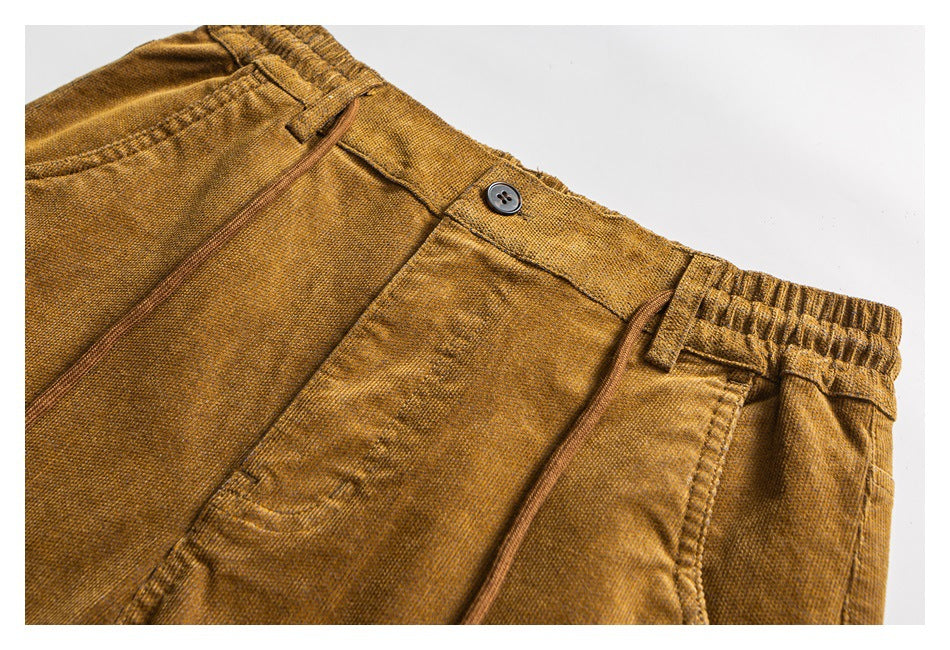 Close-up of the mustard-brown pants’ front waistband, button, drawstrings, and pocket opening.
