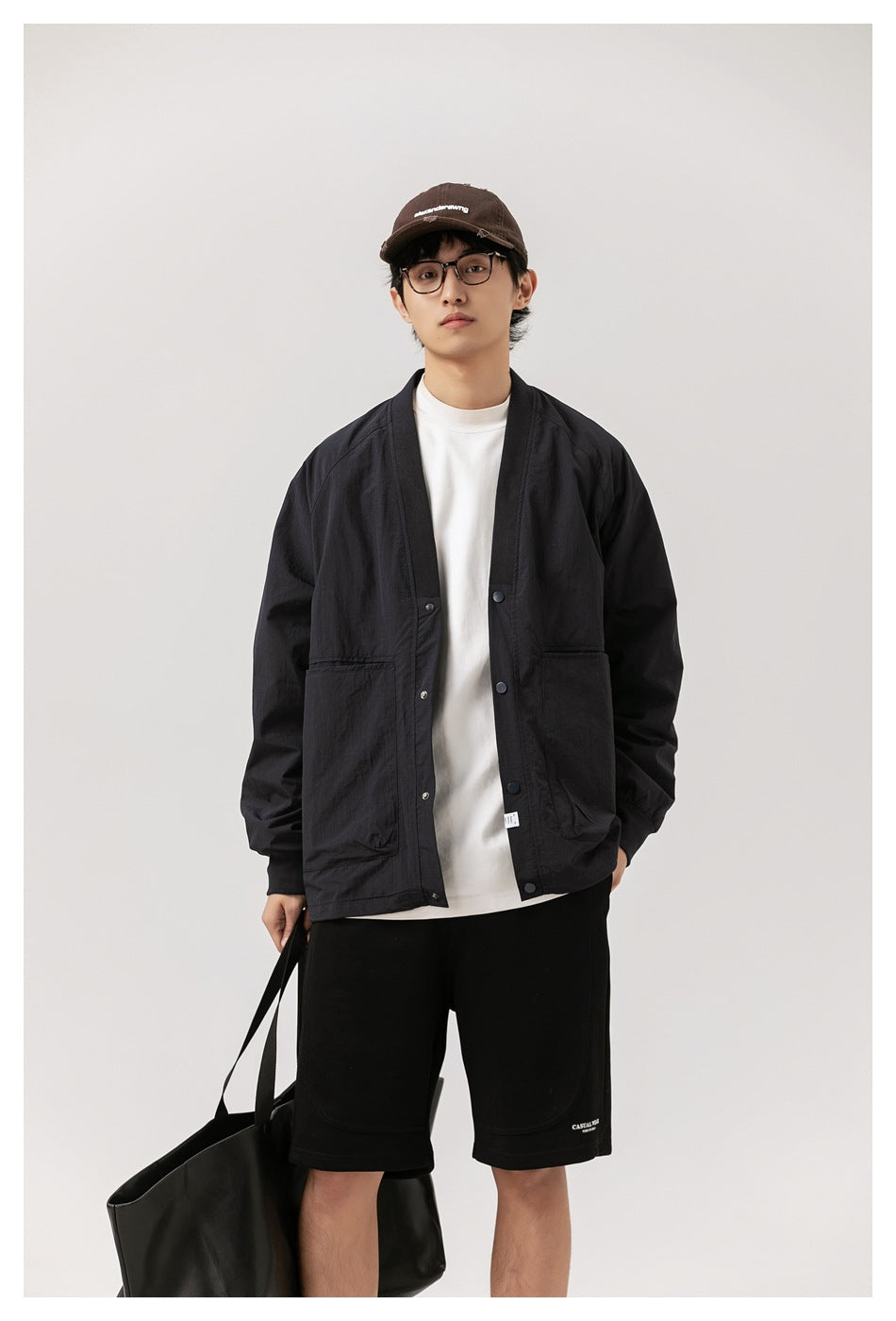 Front view of a model wearing a black snap-front jacket with large pockets over a white shirt and black shorts.