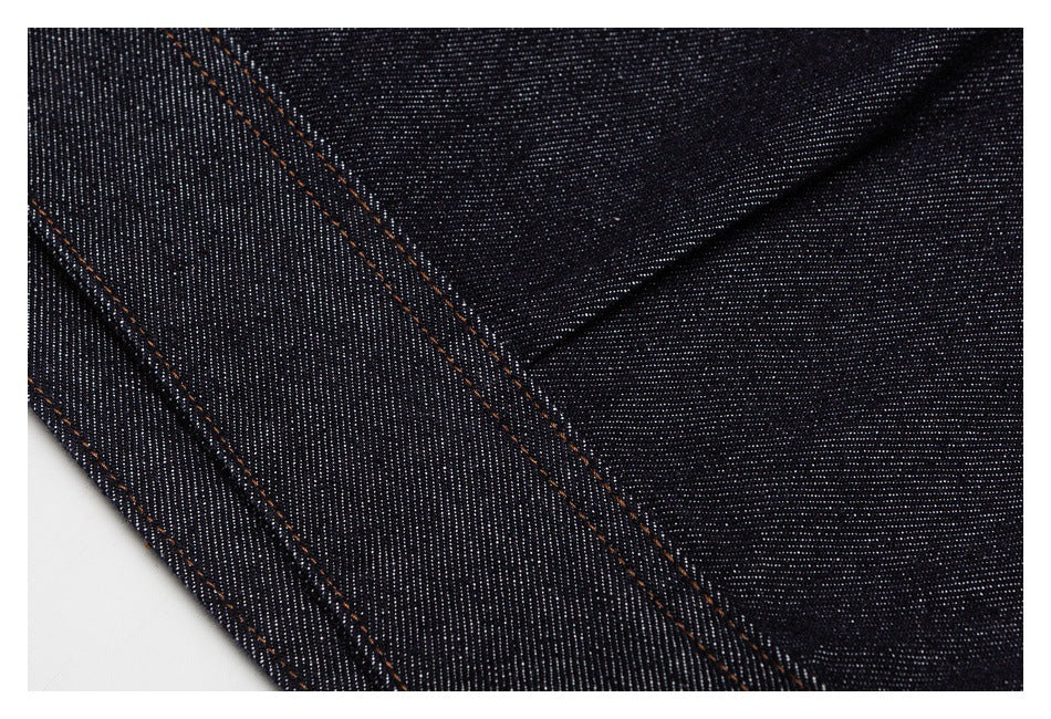 Close-up of dark indigo denim panels with parallel orange topstitched seams.
