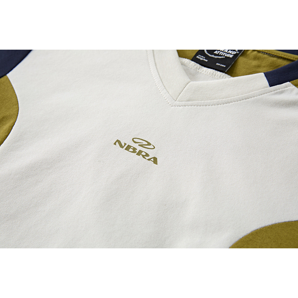 Close-up of an ivory T-shirt chest with a small olive logo and navy and olive color-block accents.